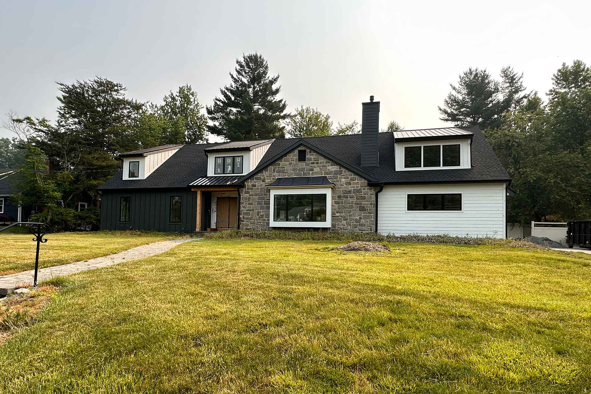 Recently developed house with contrasting dark and white panels, stone masonry, and a neatly manicured lawn at golden hour.